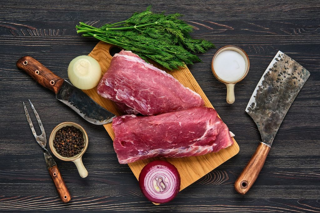 Overhead view of raw pork fillet on wooden cutting board with spice