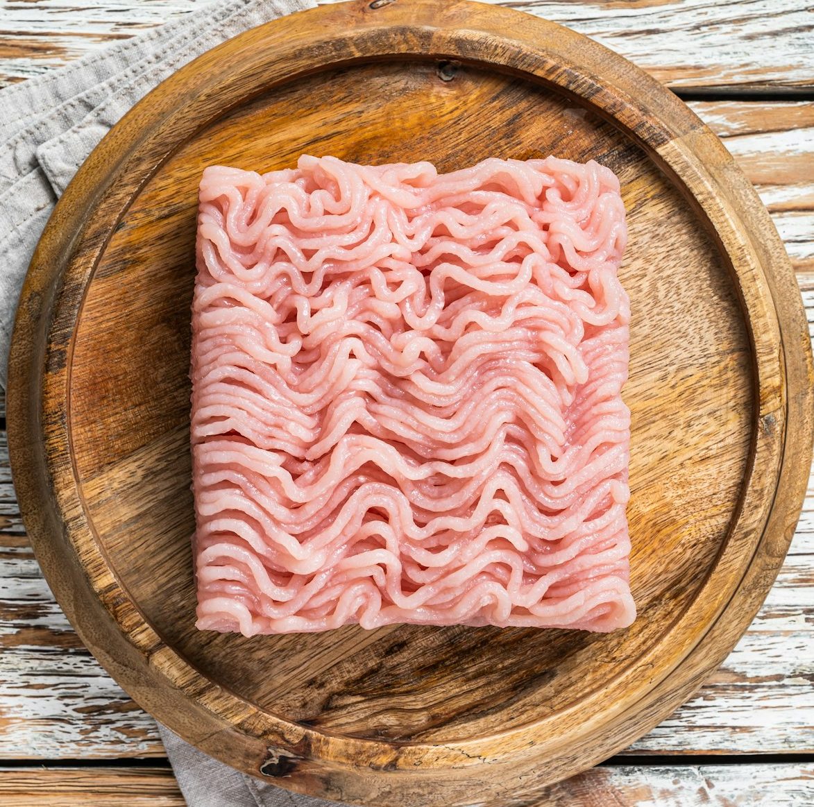 Raw mince or ground chicken meat on wooden board. White background. Top view