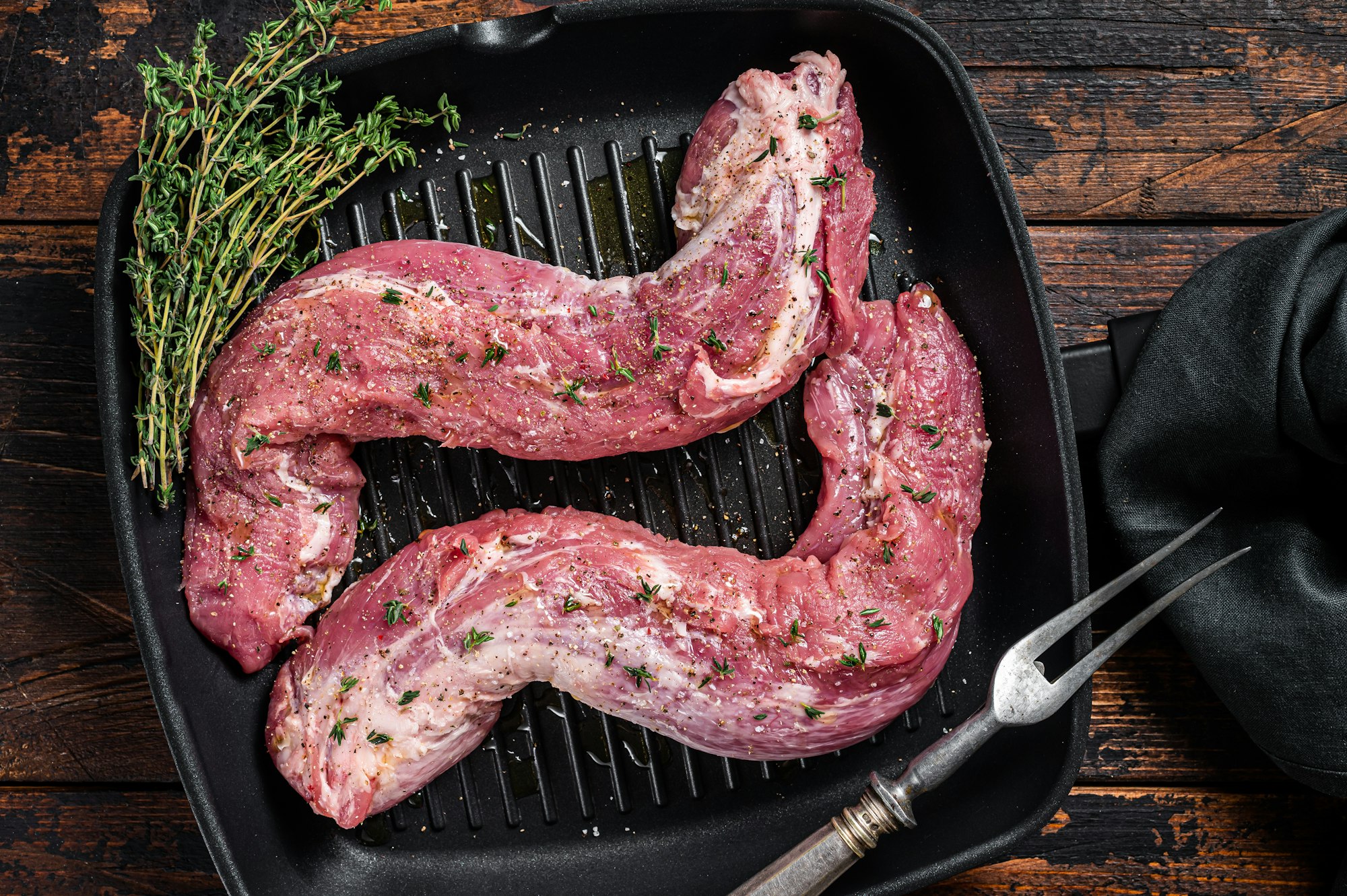 Raw Tenderloin pork fillet ready for cooking, uncooked meat in grill pan with herbs and olive oil.