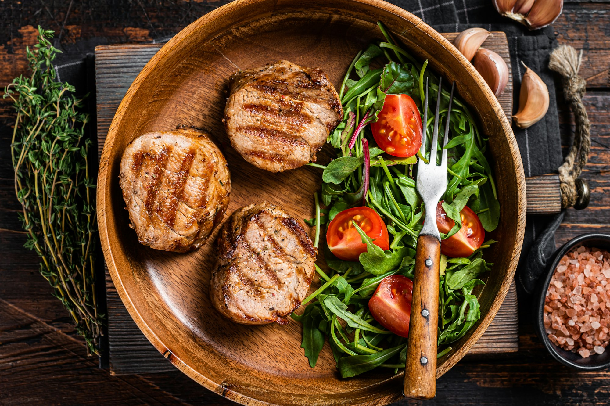 Roasted pork medallions steaks from tenderloin fillet with vegetable salad in wooden plate
